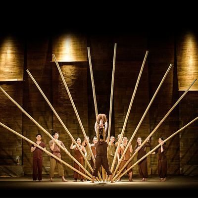 Performers raise a fan of bamboo poles around an acrobat on stage